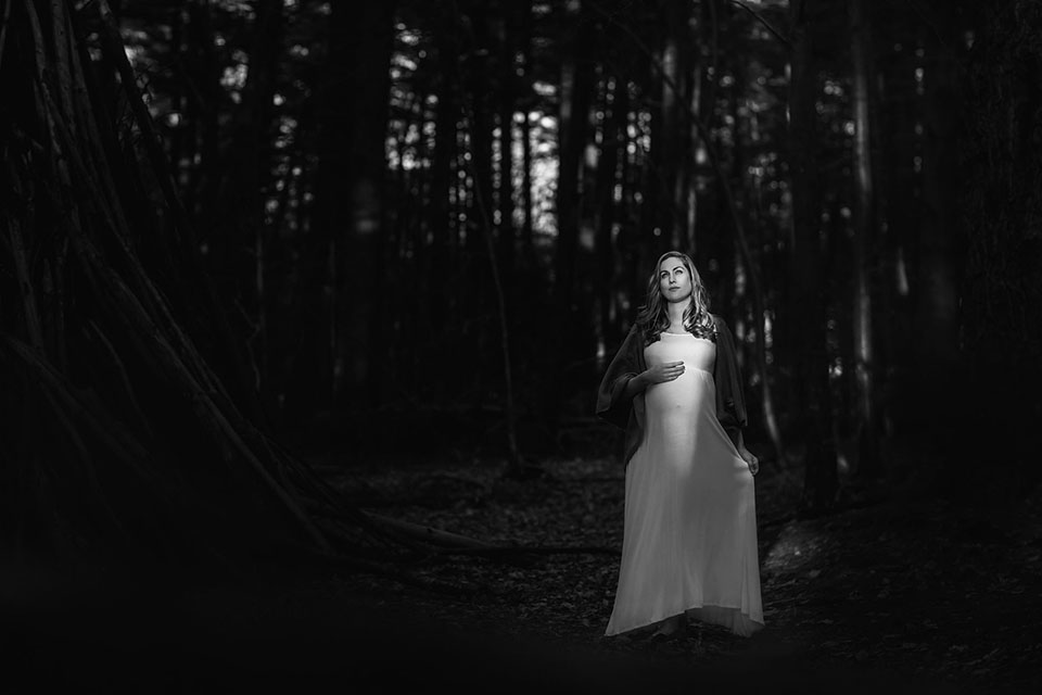 Pregnant woman taking photos in the woods in a beautiful maternity gown
