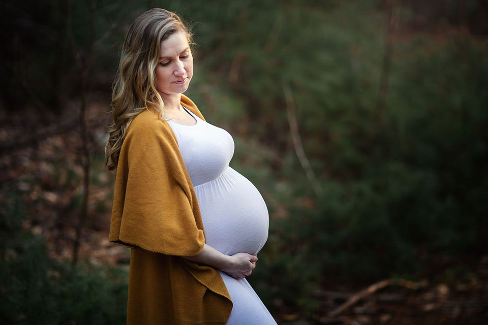Pregnant woman taking photos in the woods in a beautiful maternity gown