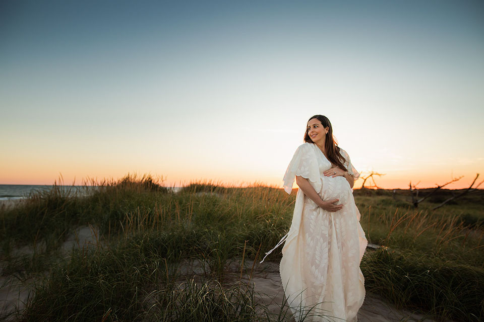 Pregnant woman taking photos on the beach in a beautiful white gown