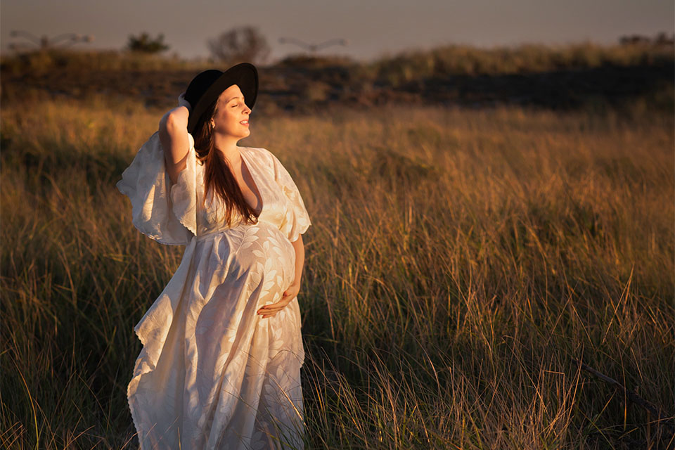 Pregnant woman taking photos on the beach in a beautiful white gown