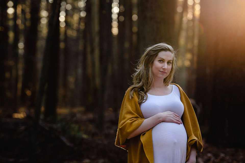 Pregnant woman taking photos in the woods in a beautiful maternity gown