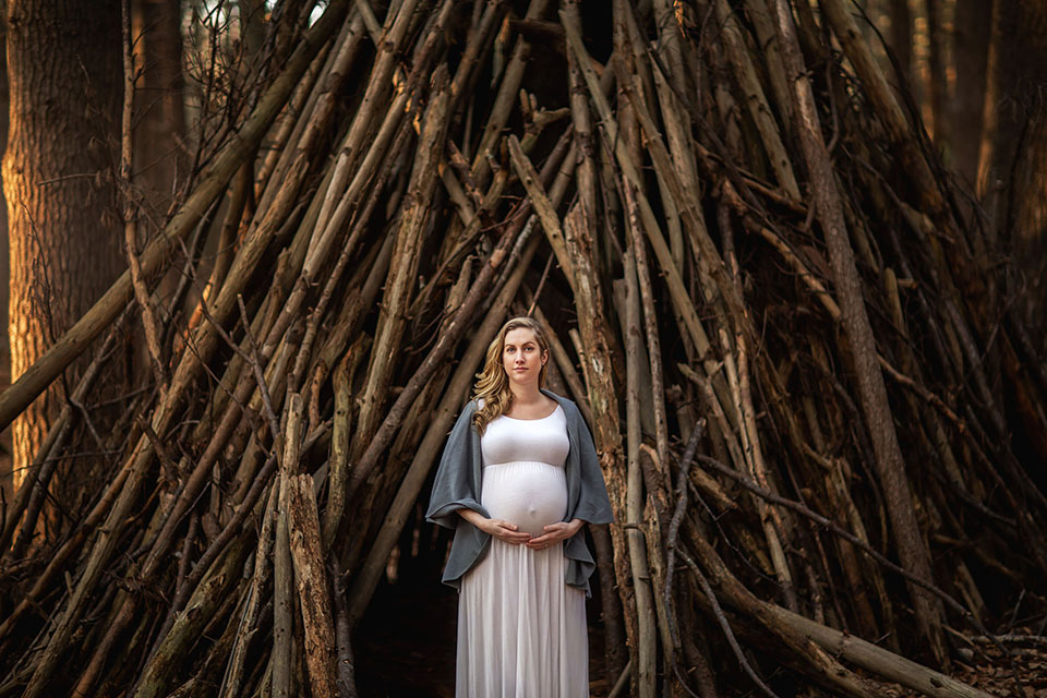 Pregnant woman taking photos in the woods in a beautiful maternity gown
