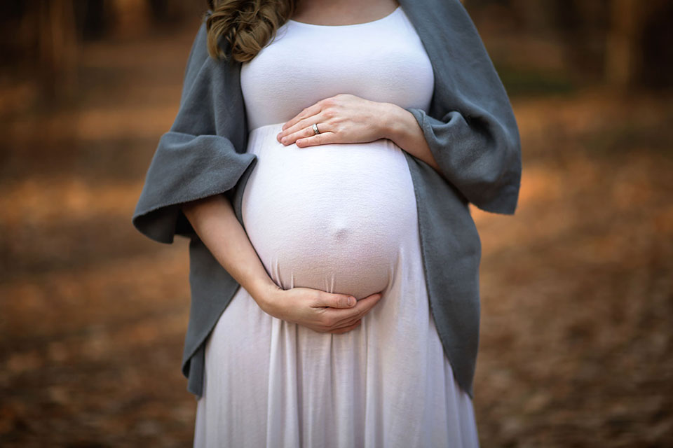Pregnant woman taking photos in the woods in a beautiful maternity gown