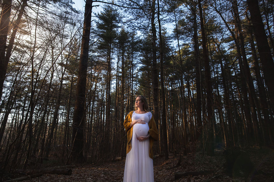 Pregnant woman taking photos in the woods in a beautiful maternity gown