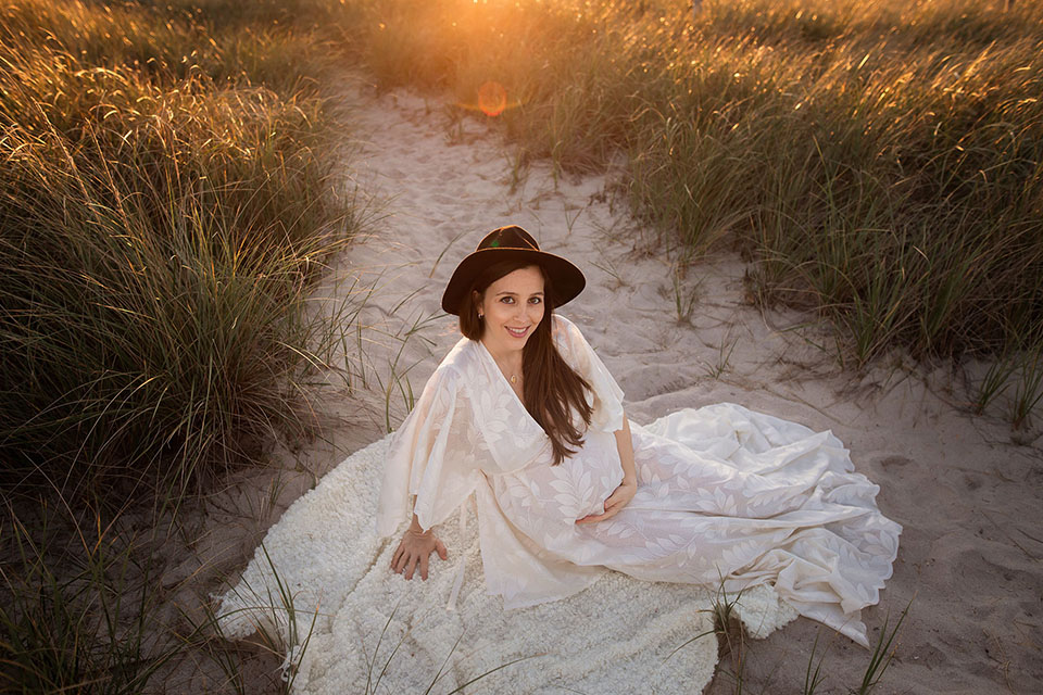 Pregnant woman taking photos on the beach in a beautiful white gown