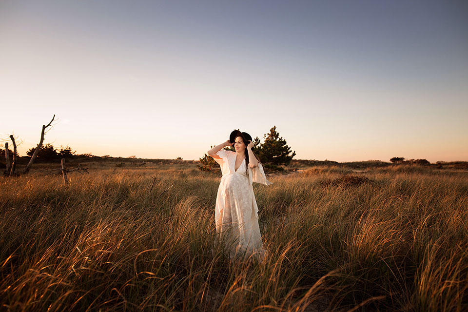 Pregnant woman taking photos on the beach in a beautiful white gown