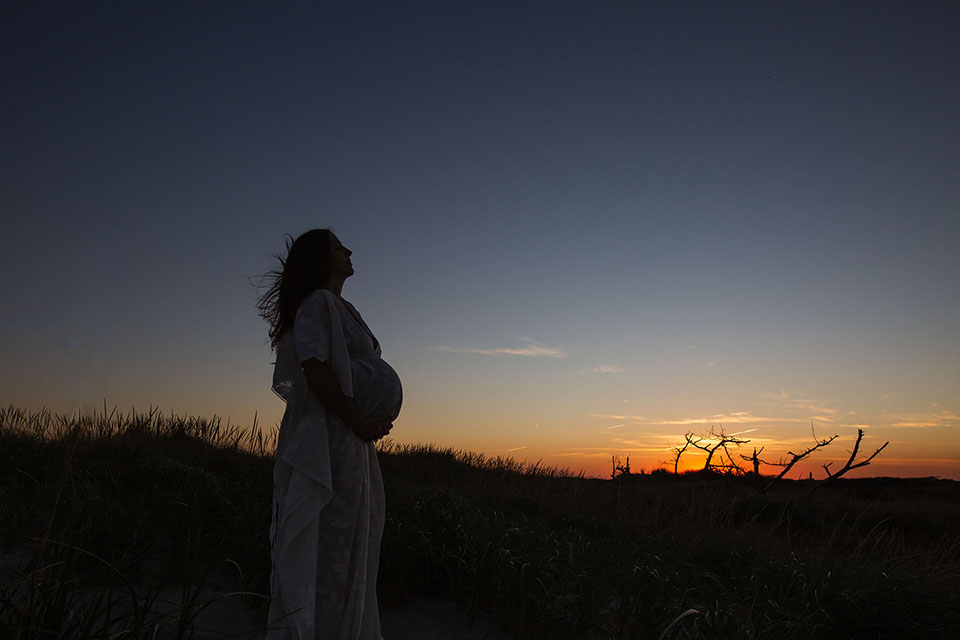 Pregnant woman taking photos on the beach in a beautiful white gown