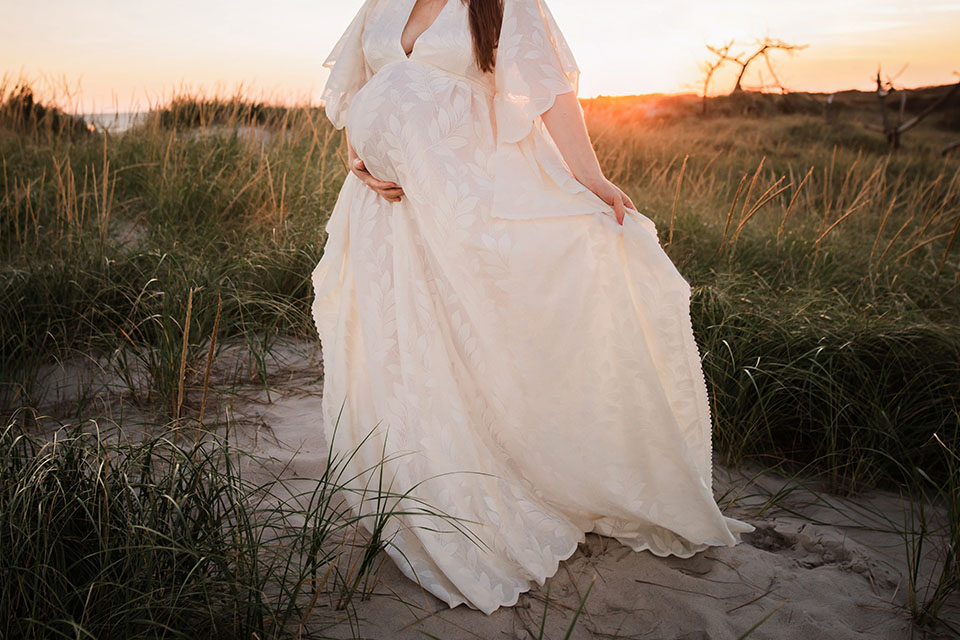 Pregnant woman taking photos on the beach in a beautiful white gown