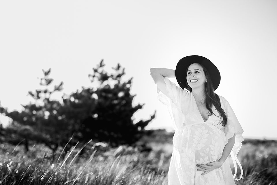 Pregnant woman taking photos on the beach in a beautiful white gown