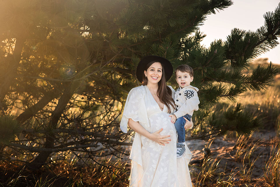 Pregnant woman taking photos on the beach in a beautiful white gown