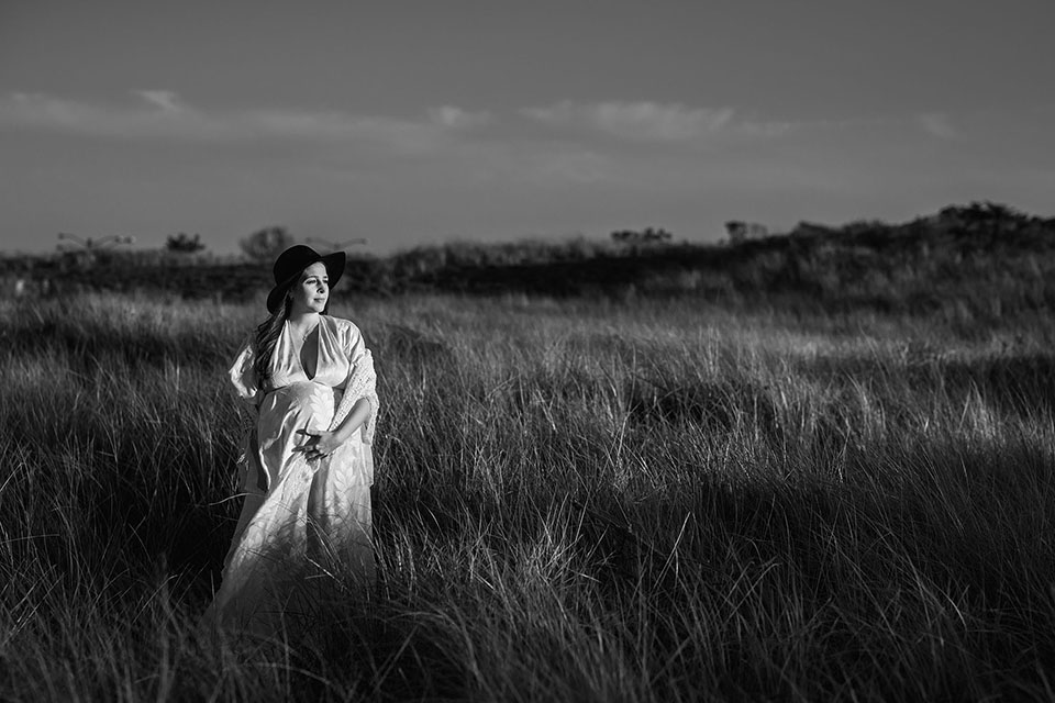 Pregnant woman taking photos on the beach in a beautiful white gown